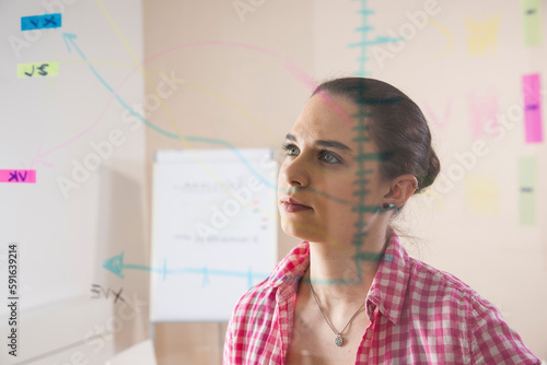 Young Businesswoman Working in Office Looking at Plans Displayed on a Glass Board photo