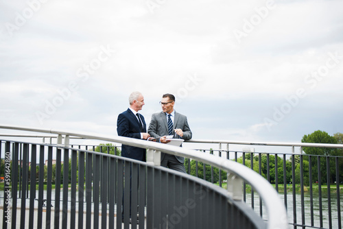 Mature businessmen standing on bridge talking, Mannheim, Germany