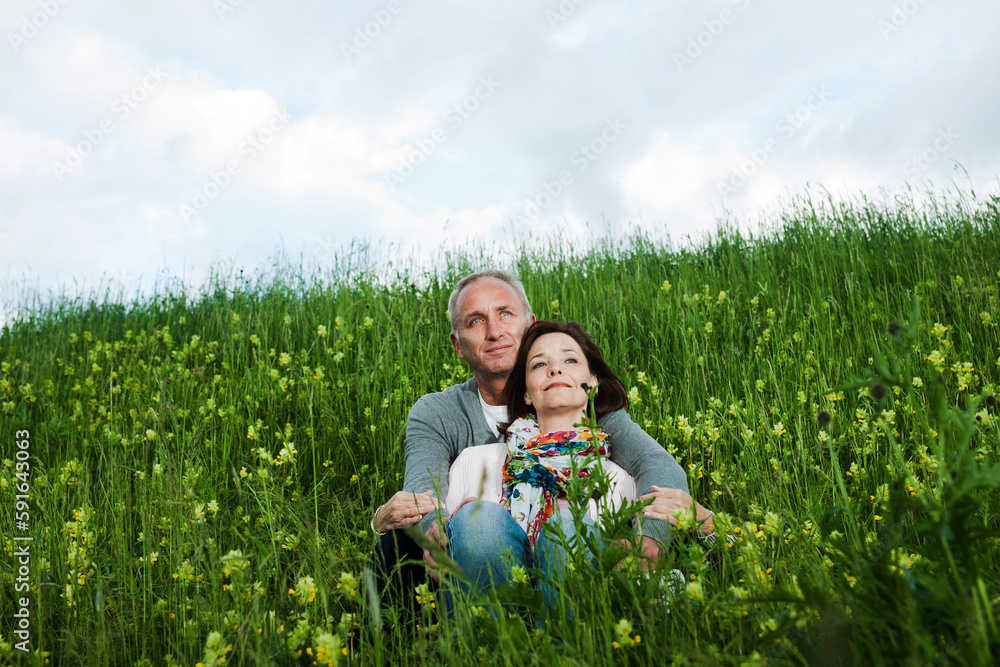 Portrait of mature couple sitting in field of grass, embracing, Germany Portrait of mature couple sitting in field of grass, embracing, Germany