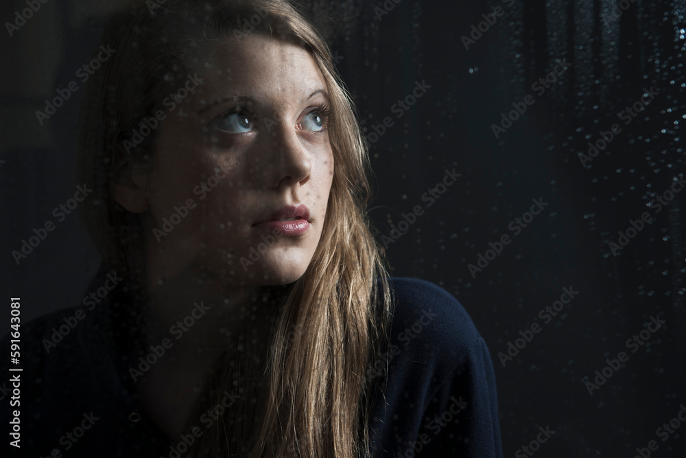 Portrait of young woman behind window, wet with raindrops, looking up Portrait of young woman behind window, wet with raindrops, looking up
