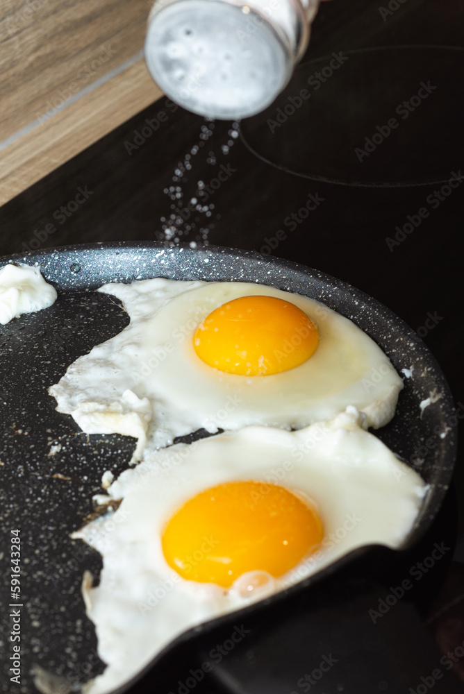 Salting of fried eggs in a frying pan on electric stove portrait view Salting of fried eggs in a frying pan on electric stove portrait view