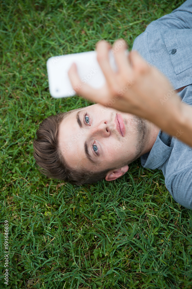 High angle view of young man lying on grass, looking at cell phone, Germany High angle view of young man lying on grass, looking at cell phone, Germany