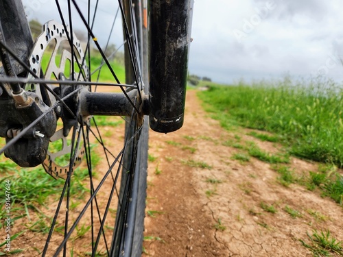 Close up of bicycle wheel on dirt road with green grass background