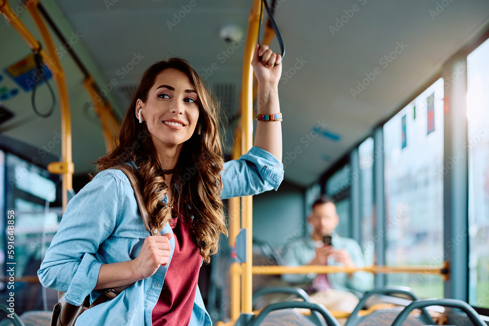 Young smiling woman holds onto handle while traveling by public bus. Young smiling woman holds onto handle while traveling by public bus.