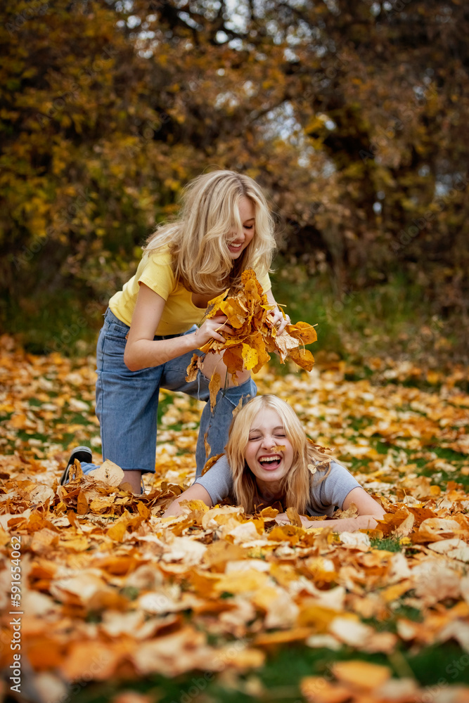Two teenage girls playing with the leaves and having fun in a city park on a warm fall afternoon; St. Albert, Alberta, Canada. Two teenage girls playing with the leaves and having fun in a city park on a warm fall afternoon; St. Albert, Alberta, Canada.
