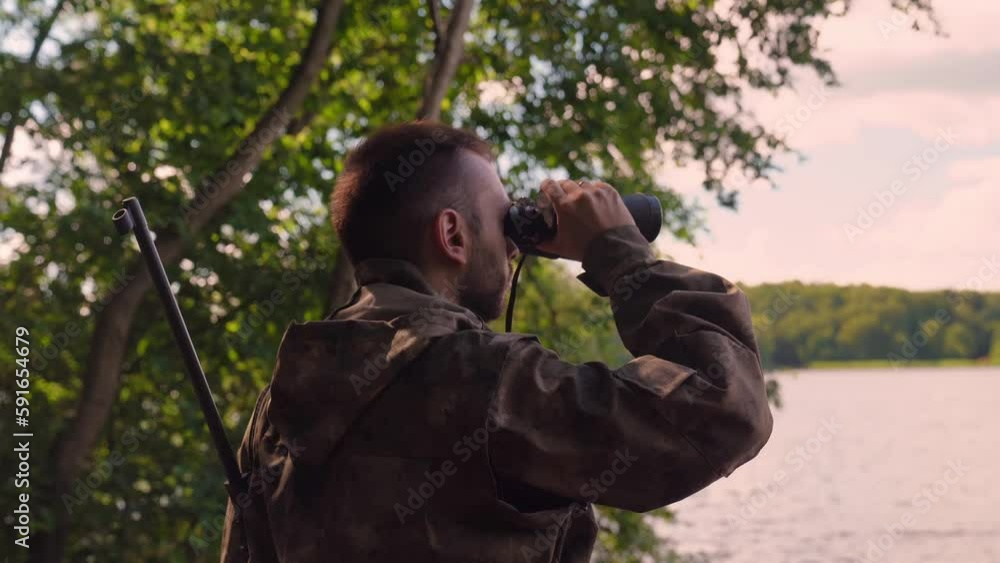 Ranger or hunter with binocular observing forest. young soldier walking through Forest near lake Ranger or hunter with binocular observing forest. young soldier walking through Forest near lake