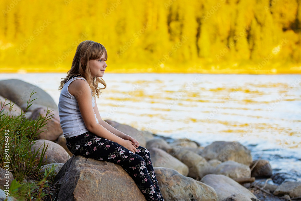 Outdoor portrait of a girl sitting by a water in autumn; Edmonton, Alberta, Canada Outdoor portrait of a girl sitting by a water in autumn; Edmonton, Alberta, Canada