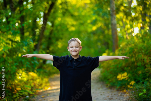 Outdoor portrait of a young boy standing on a park trail with arms outstretched; Edmonton, Alberta, Canada