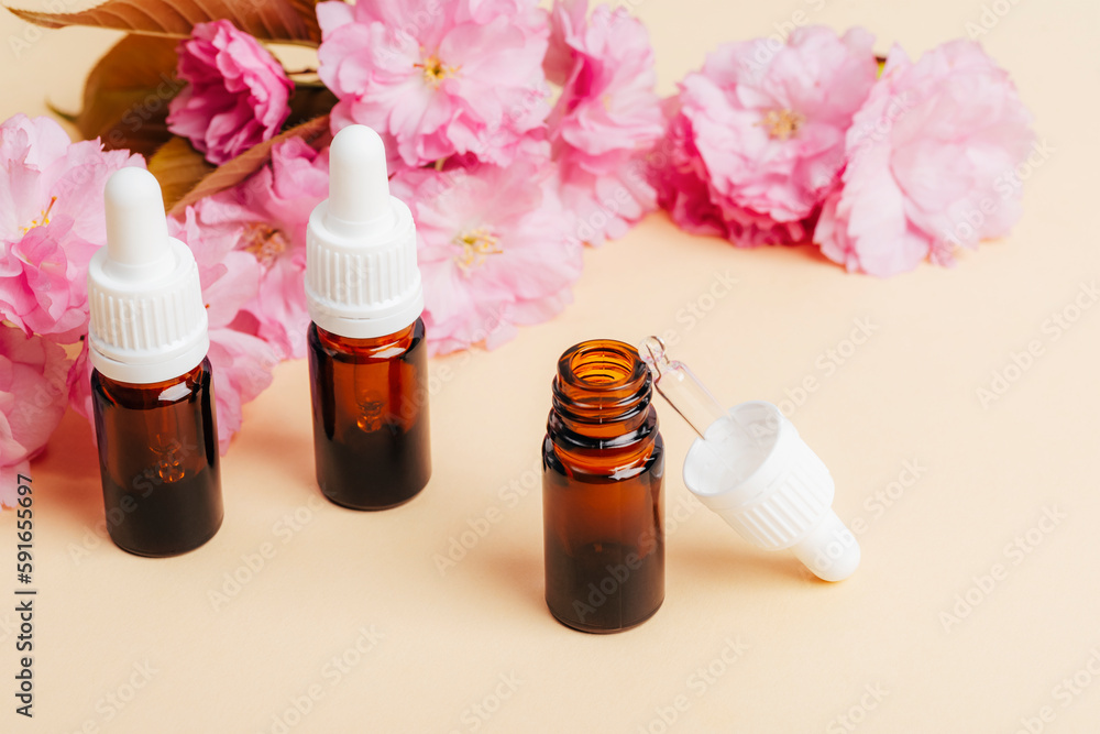 Brown glass bottles with essential oil and pink cherry blossom on beige background. Aromatherapy, beauty treatment concept. Closeup Brown glass bottles with essential oil and pink cherry blossom on beige background. Aromatherapy, beauty treatment concept. Closeup