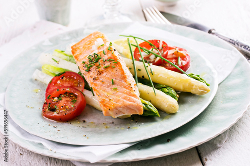 Traditional German green and white asparagus with salmon, potatoes and tomatoes served as close-up on a design plate