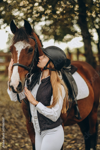 A young female equestrian stands near her horse and prepares for a competition.