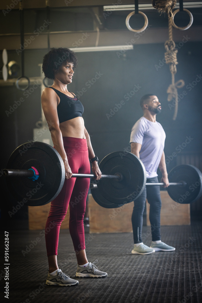 Dedicated biracial young man and woman lifting barbells while standing in gym, copy space Dedicated biracial young man and woman lifting barbells while standing in gym, copy space