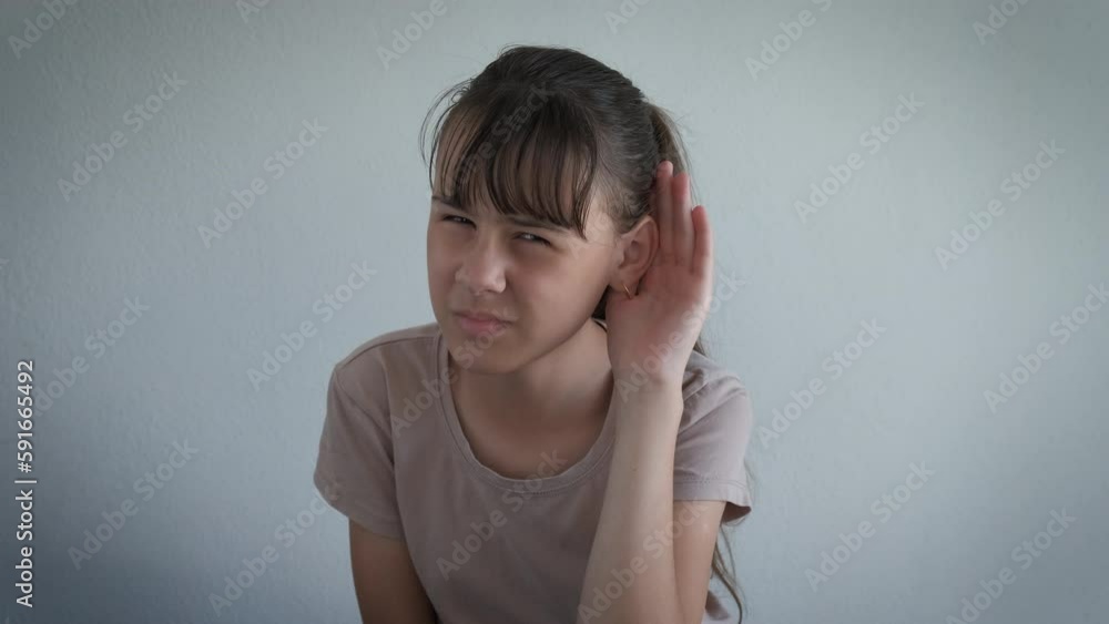 Child with deafness problems indoor. An annoyed upset teen girl keep her hand by the ear for better hearing in the room. Child with deafness problems indoor. An annoyed upset teen girl keep her hand by the ear for better hearing in the room.
