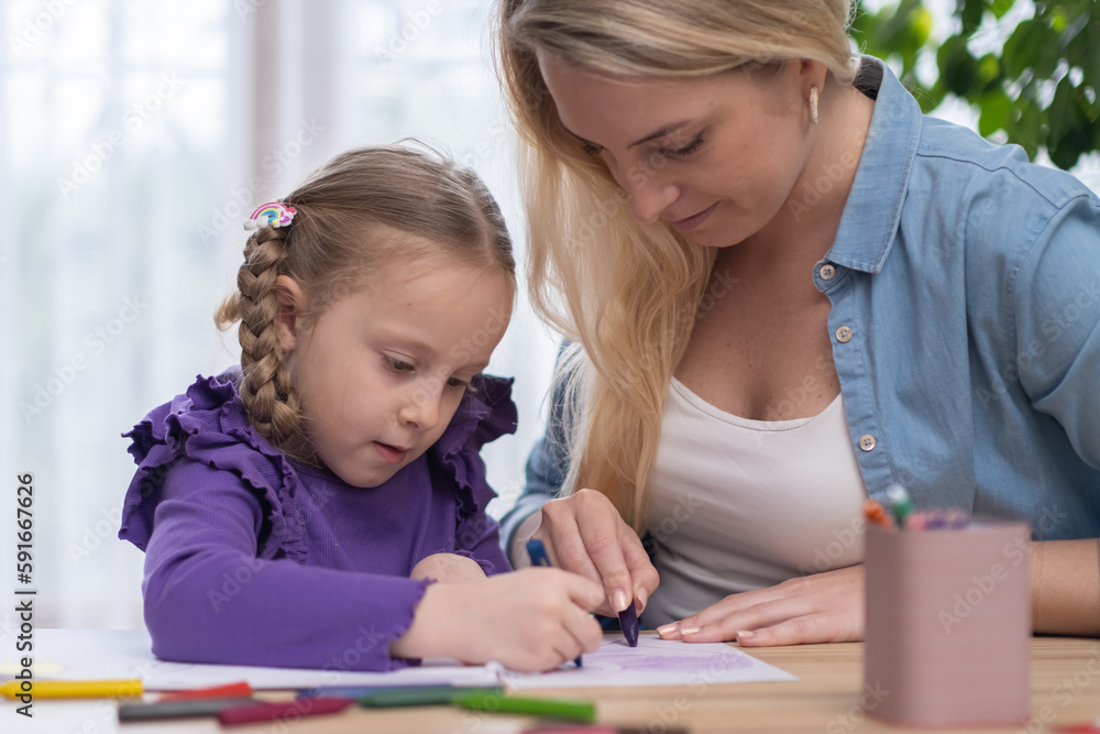 Mother helping to daugher with homework, they working on school assignment together sitting at desk drawing picture with color pensils. Mother helping to daugher with homework, they working on school assignment together sitting at desk drawing picture with color pensils.