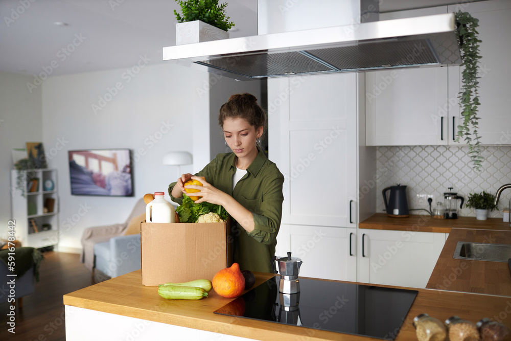 Waist up portrait of modern young woman unpacking fresh groceries in minimal kitchen interior, copy space