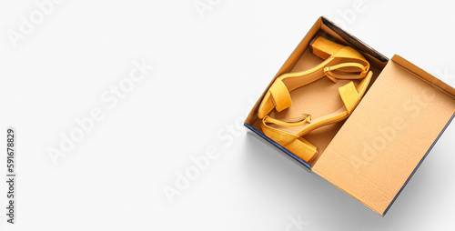 Cardboard box with high heeled sandals on light background with space for text