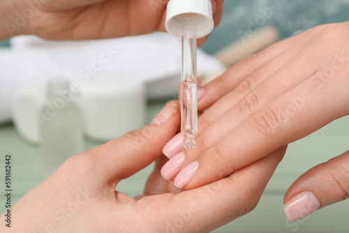 Manicure master applying cuticle oil onto female fingernails  closeup