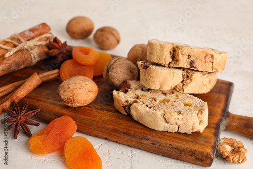 Wooden board with tasty biscotti cookies, walnuts, dried apricots and spices on light background, closeup