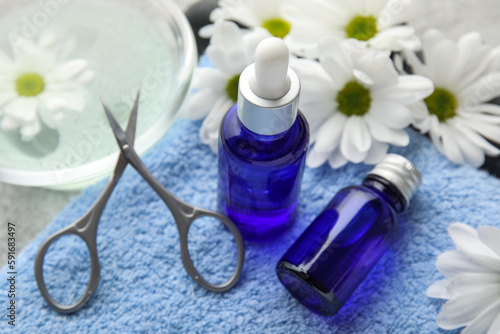 Bottles of cuticle oil, towel, manicure scissors and chamomile flowers, closeup