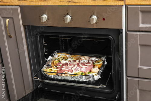 Baking dish with raw meat and vegetables in oven