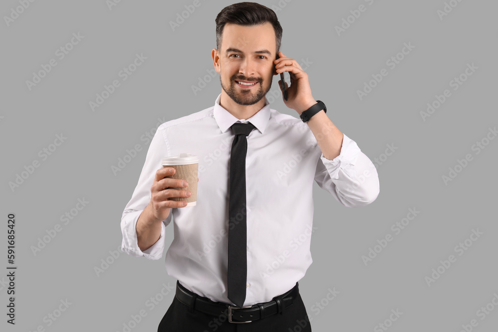 Handsome businessman with cup of coffee talking by mobile phone on grey background Handsome businessman with cup of coffee talking by mobile phone on grey background