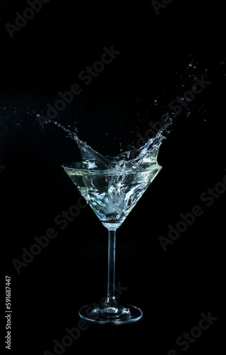 Glass with splashing martini on black background