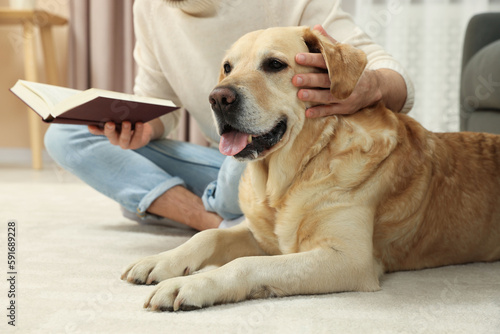 Man reading book on floor near his cute Labrador Retriever at home, closeup