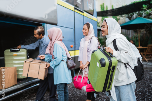 happy asian muslim passengers with their parent traveling by bus. portrait of family are putting suitcases into bus trunk baggage