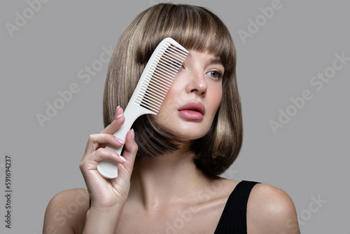 Portrait of a beautiful brown-haired woman holding a comb in her hand. Shiny short hair. Gray background.