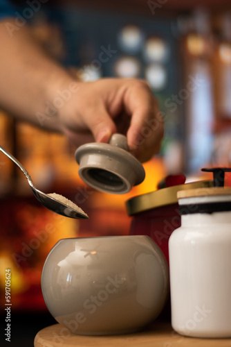 Vertical view of Hand taking sugar from Mugs of sugar and containers over a table in night restaurant