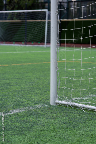 A white aluminum goal with a white net for youth   s football tournament on artificial plastic grass pitch in the morning waiting for teams to play and practice. Another white goal in a background.