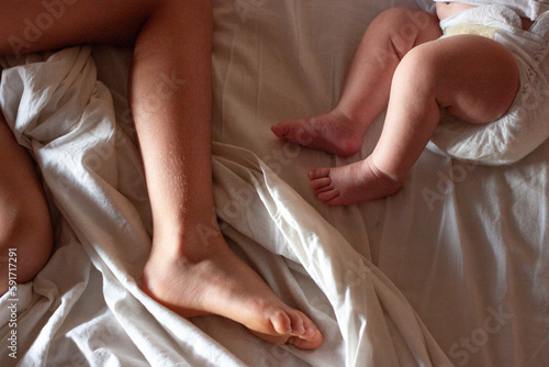 upper view on feet of elder child and newborn baby on the bed