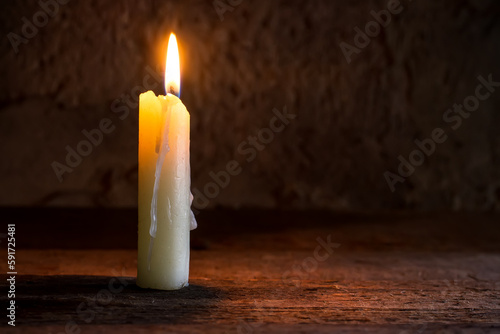 A burning candle on a rough wooden shelf. A lit candle in the twilight.