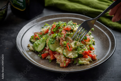 Quinoa and vegetable salad. A human hand picks a salad with a fork.