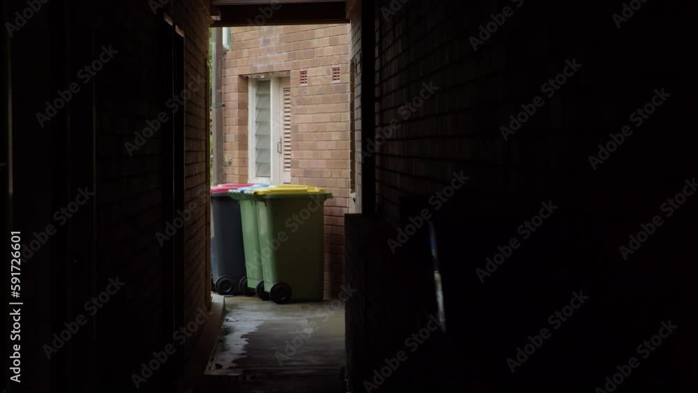 Some rubbish bins are seen at the end of a dark walkway. Some rubbish bins are seen at the end of a dark walkway.