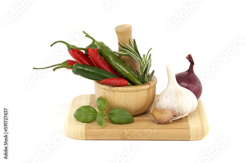 Chili peppers in wooden mortar and herbs over white