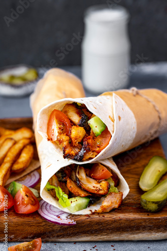 Chicken doner kebab wraps on a wooden board accompanied by chips, pickles, tomatoes on the side and a glass of ayran yogurt drink behind them. photo