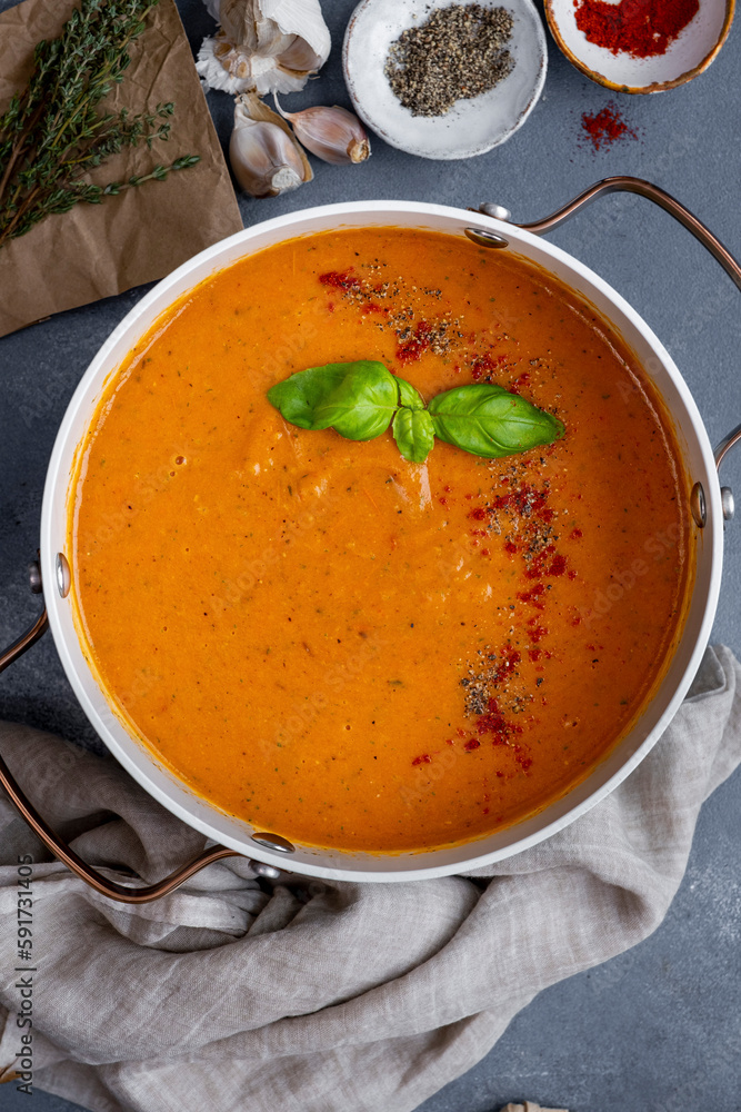 Roasted tomato soup garnished with spices and fresh basil leaves in a pot, black pepper, paprika, garlic and thyme on the side. Roasted tomato soup garnished with spices and fresh basil leaves in a pot, black pepper, paprika, garlic and thyme on the side.