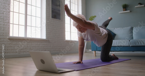 Senior caucasian woman stretching at home. Mature athlete watching online stream on laptop and exercising - healthy lifestyle, wellbeing 