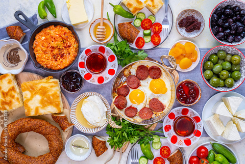 Flat-lay of Turkish breakfast with egg dishes in copper pan, pastries like borek and simit, jams, olives, cheese, vegetables and Turkish tea in traditional tulip glasses. photo