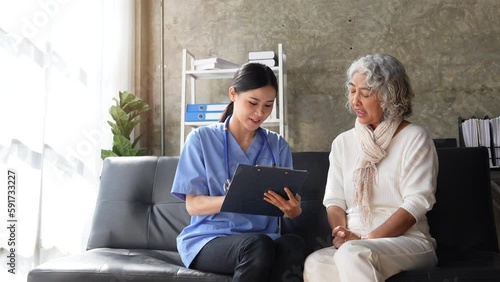 Young nurse and senior woman going through medical record on clipboard during home visit