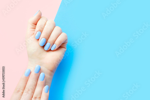 Female hands with light blue manicure on blue and pink background with copy space.