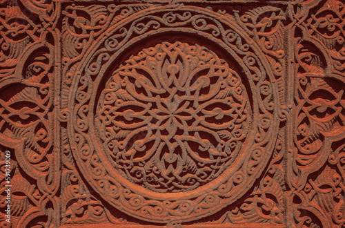 Carved round ornament with intertwining strips forming a pattern placed in a round frame on a red volcanic stone. Traditional tufa stone carving ornament on a wall of Armenian Orthodox Church. © Maxim Chuev