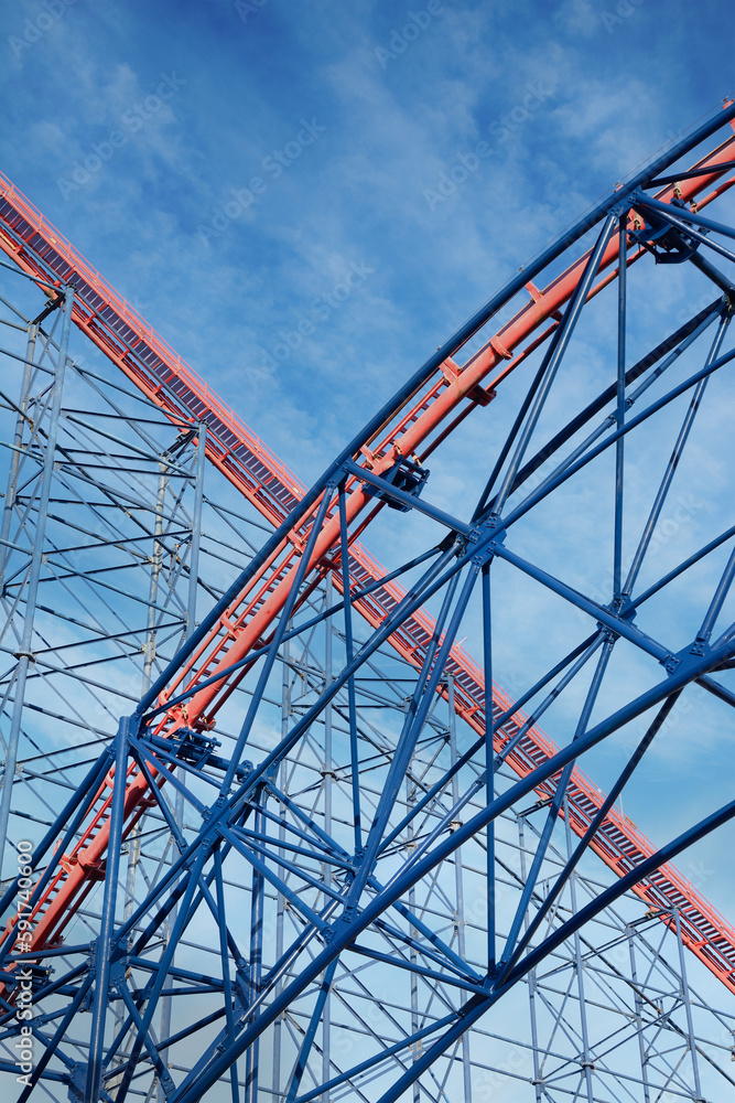 section of a red and blue roller coaster against a blue sky