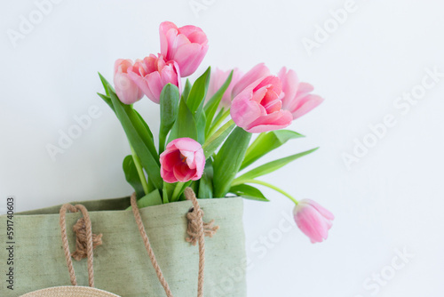 Pink tulips bouquet in green shopping bag on white background copy space