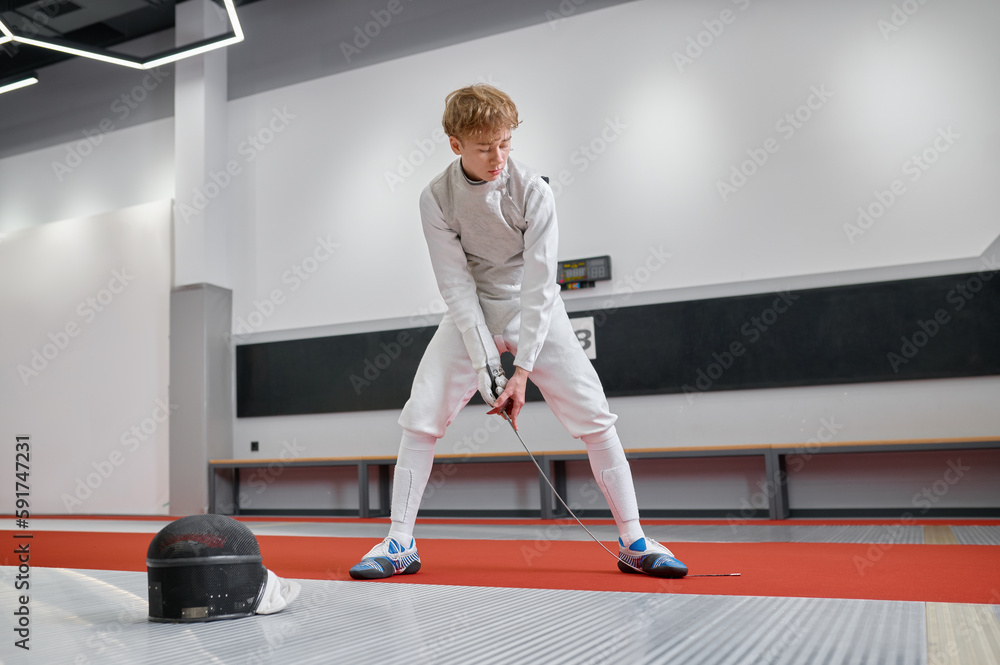 Teenage boy wearing fencing costume checking strength of blade