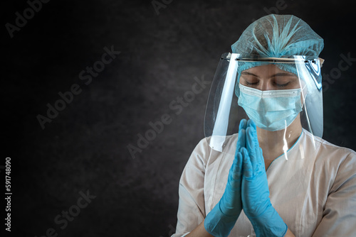 Young feamle doctor in uniform prays for God's, isolated on dark, studio shot photo