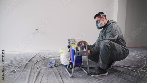 Male builder painter setting up machine for airless wall spray painting. Finishing inside buildings photo