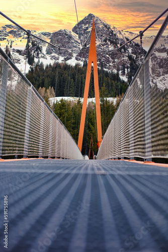 Unendlich lange orangene Talbrücke vor einem im Abendlicht erscheinendem Himmel vor einer Wand von in sattem grün erscheinenden Bäumen photo