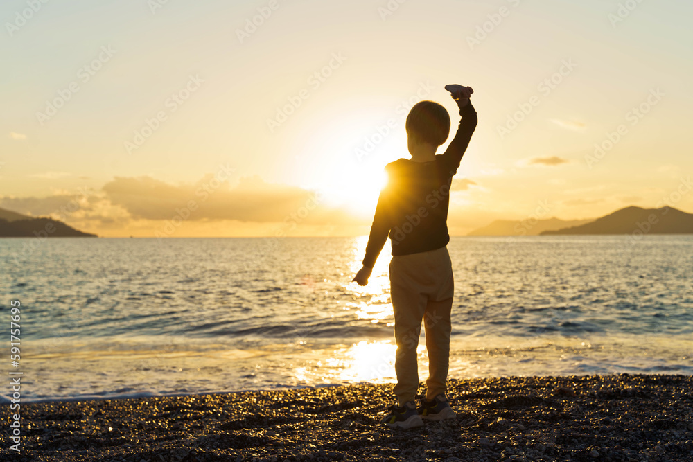 Silhouette of little boy on the beach at sunset.